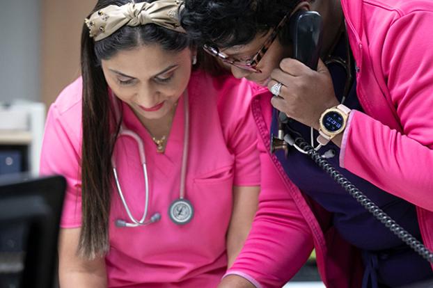 Two nurses conversing while reviewing a patient chart.