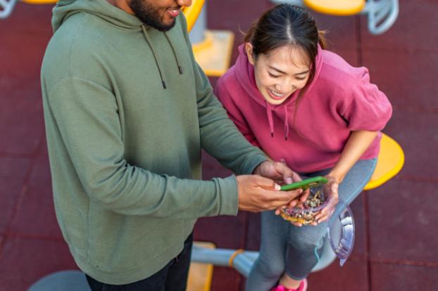 Couple in athletic wear looking at phone and eating a snack.