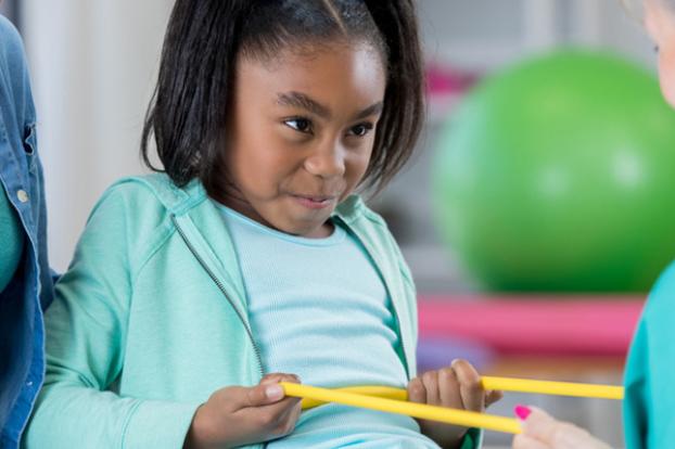 Child stretching a band with parent and therapist assisting