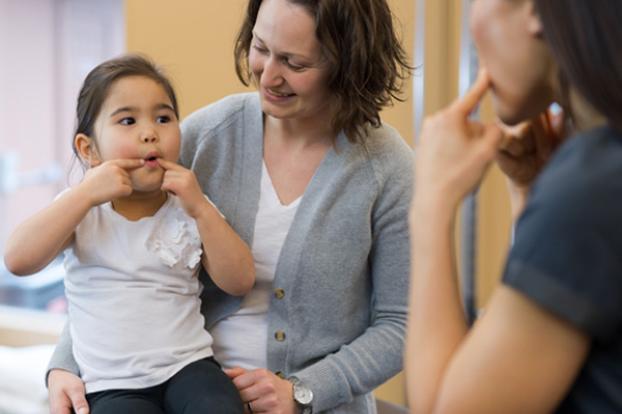 Child holding cheeks with parent and therapist