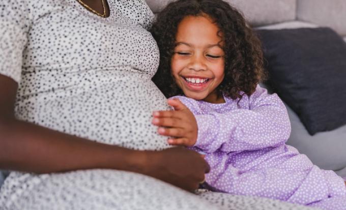 Younger sibling hand on mom's pregnant tummy.