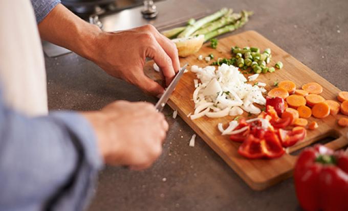 Closeup of hands chopping vegetables on wood cutting board.