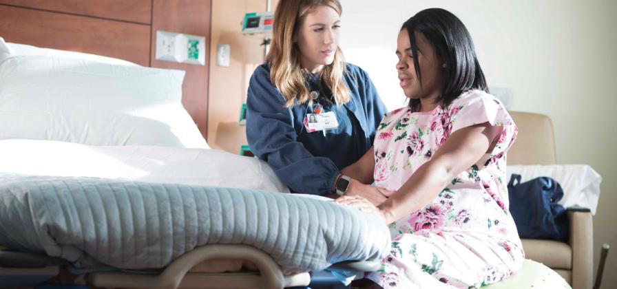 Labor sitting on ball near bed with nurse near.