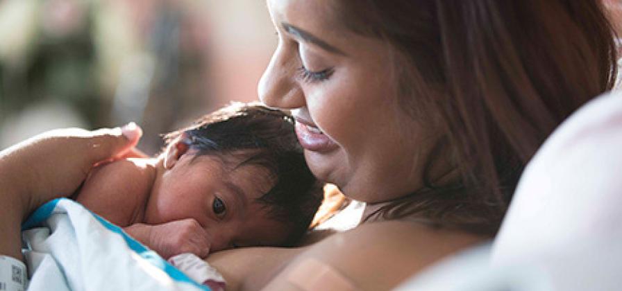 New mother holding newborn infant in hospital bed.