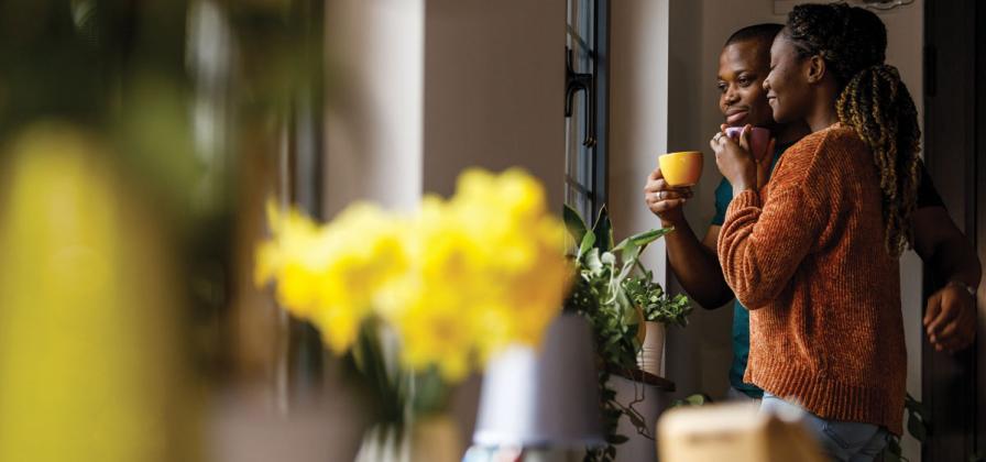 Couple looking our window daffodils on table.