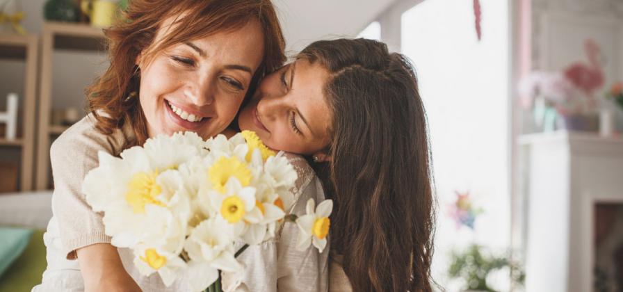 Daughter hugging mom with daffodil bouquet.