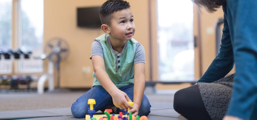 Child with physical therapist and blocks on the floor.