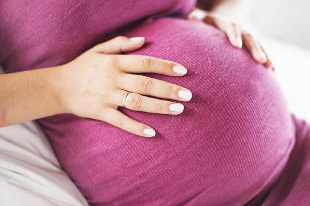 Hands on pink shirt of pregnant belly.