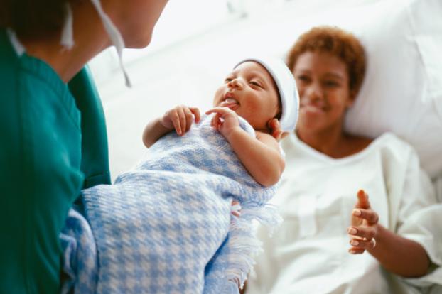 Nurse handing newborn infant to new mom.