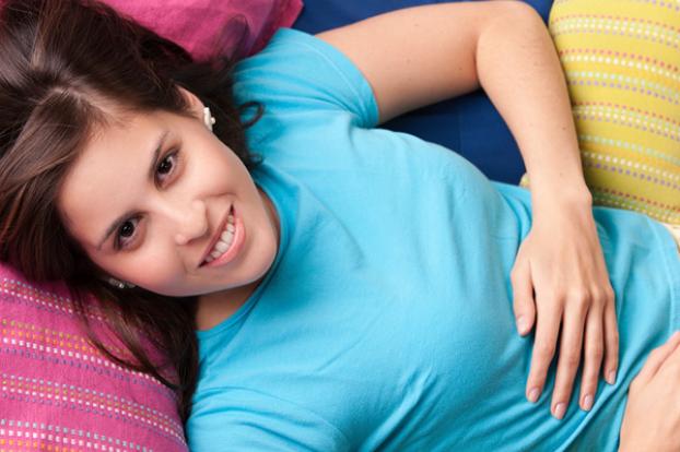 Woman hand on tummy in cyan shirt.